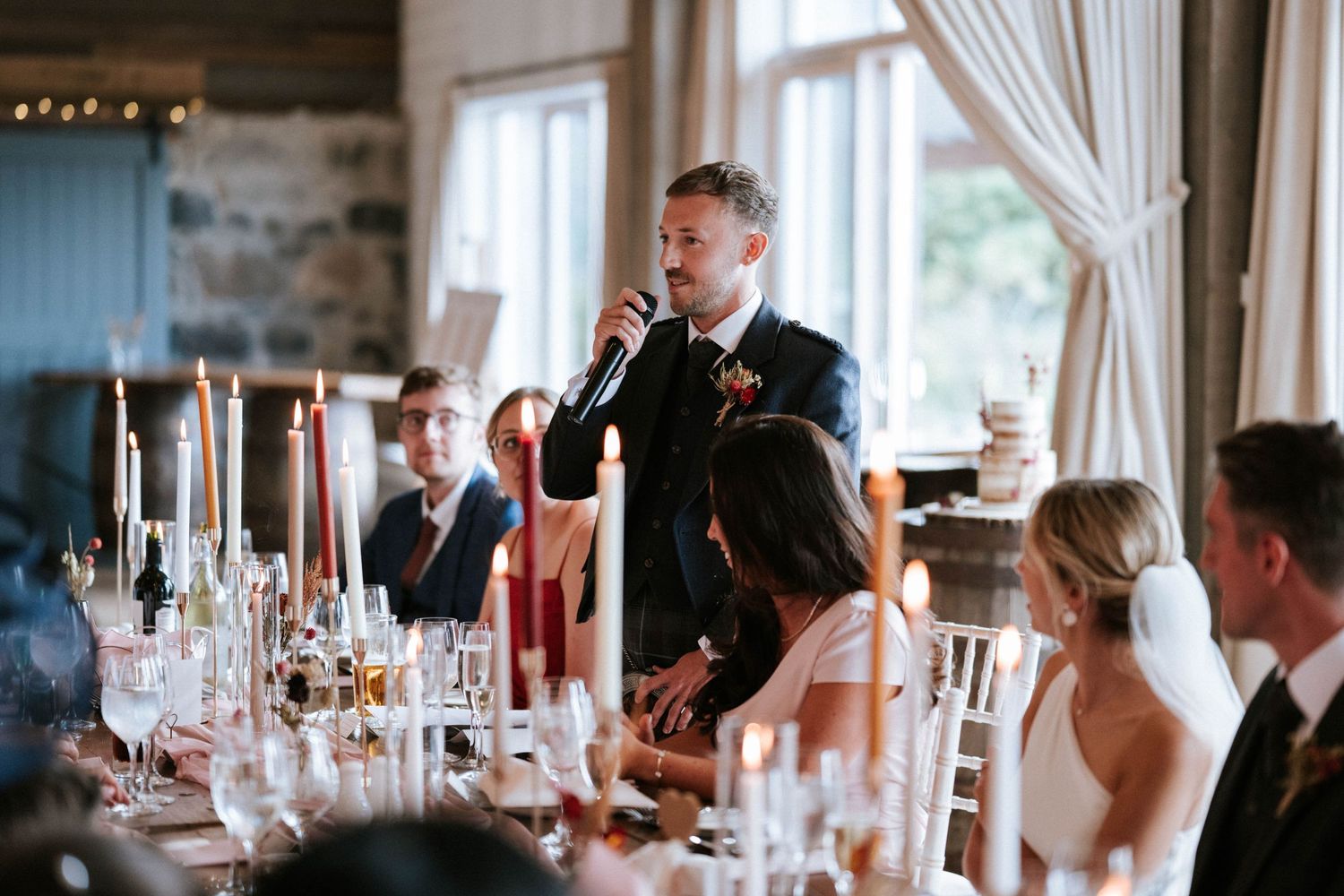 Wedding speech being delivered at reception dinner with formal table settings and candlelight.