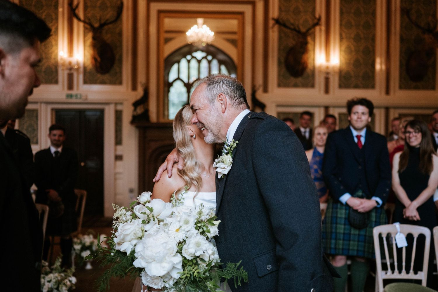 Wedding ceremony in a grand hall with ornate architectural details and chandeliers.