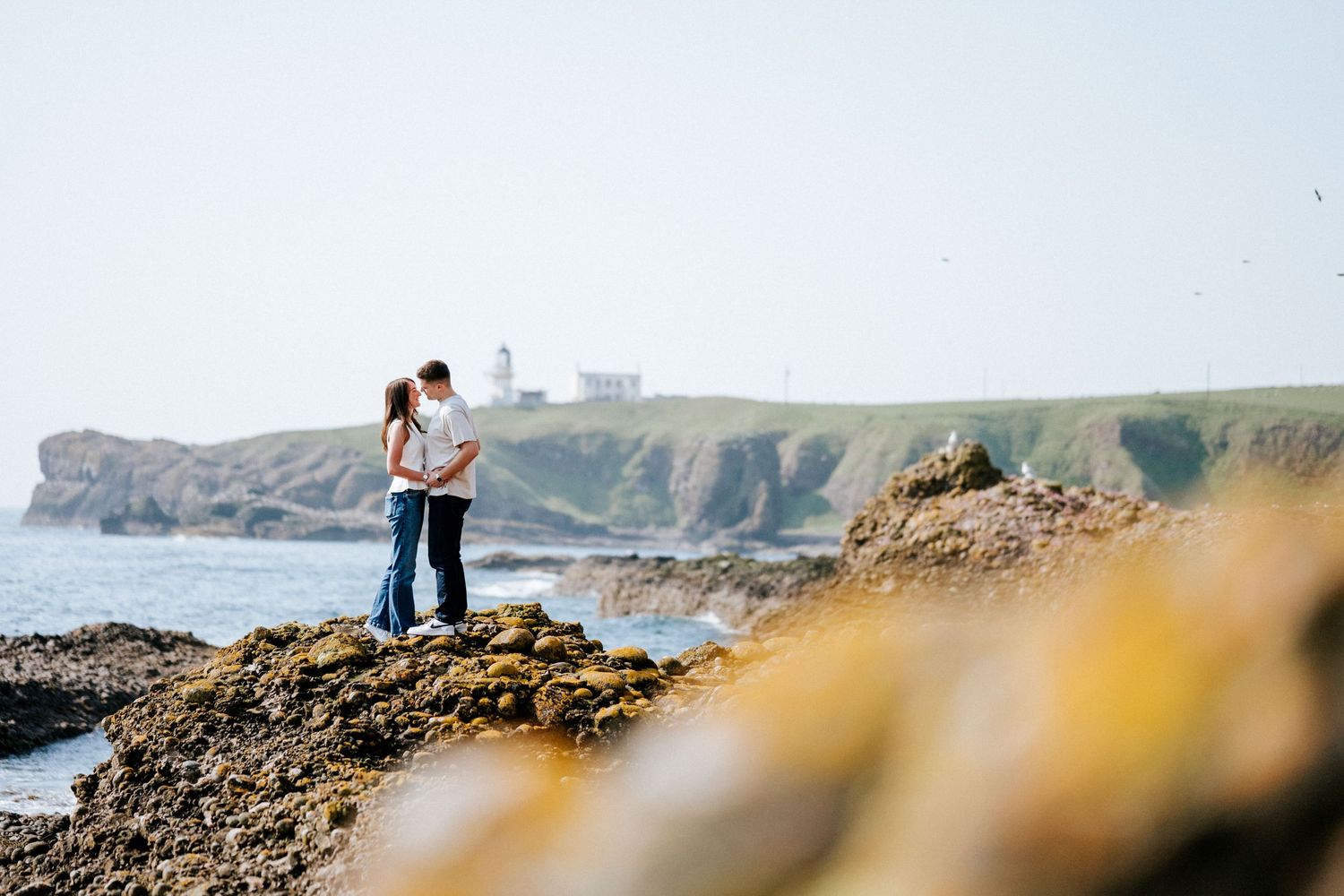 Engagement photography session Aberdeen. Distant figures walk along a rocky coastal shoreline at sunset.
