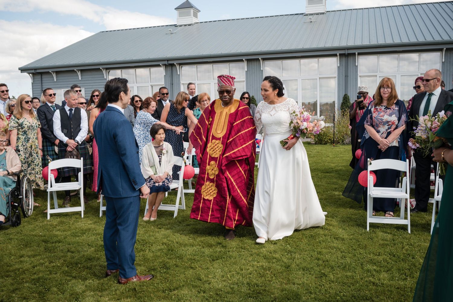 Outdoor wedding ceremony setup with white chairs and barn in background on a sunny day.