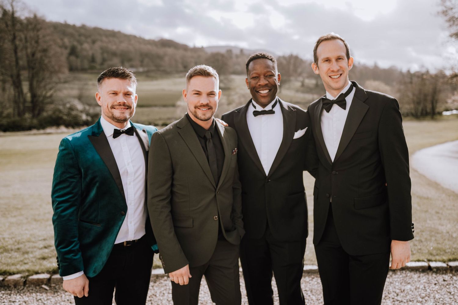 Logie House Wedding Photography. Wedding party members in black tuxedos and one in green velvet pose together outdoors.