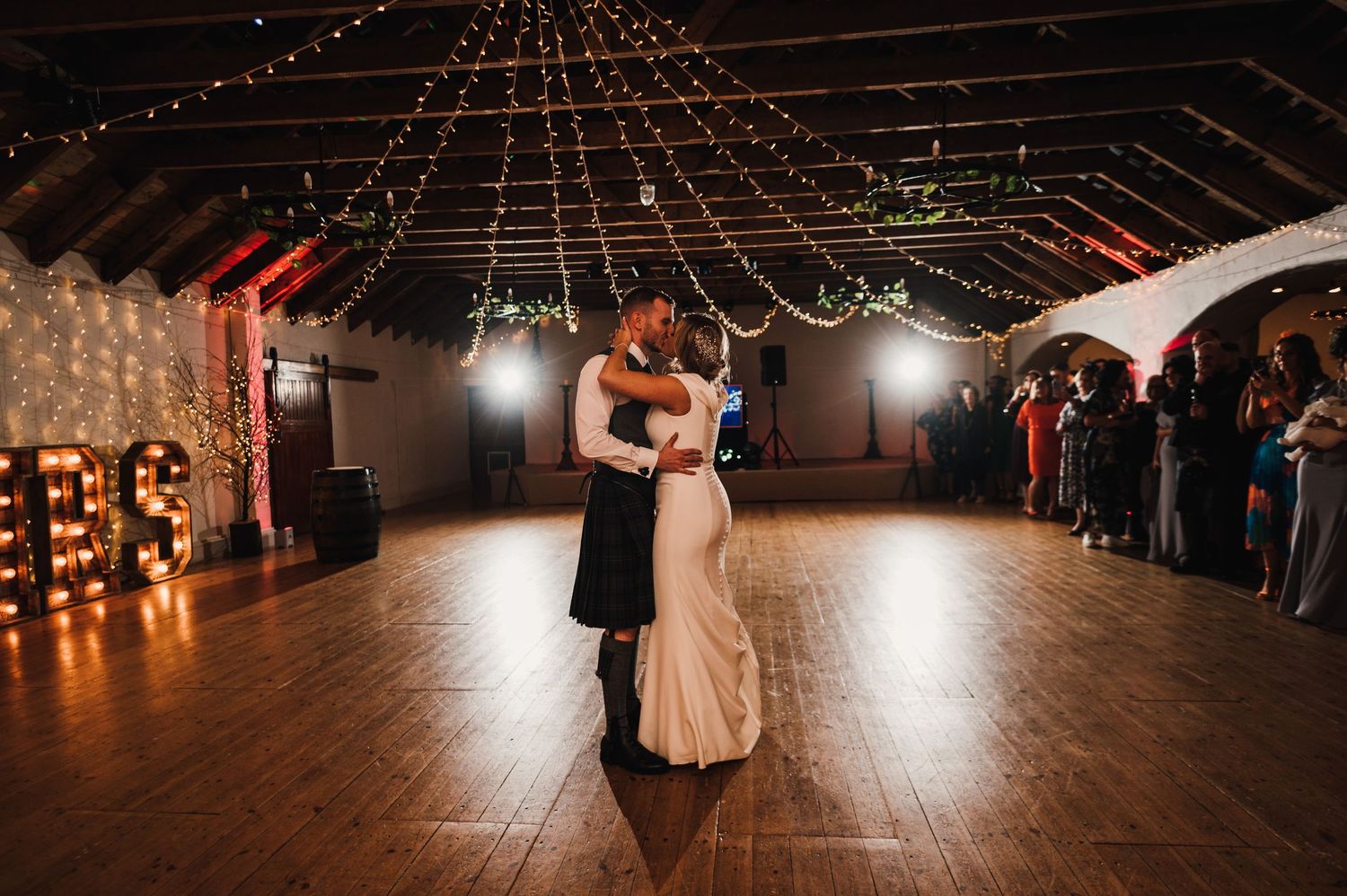 First dance in a rustic barn venue decorated with string lights and romantic ambient lighting.