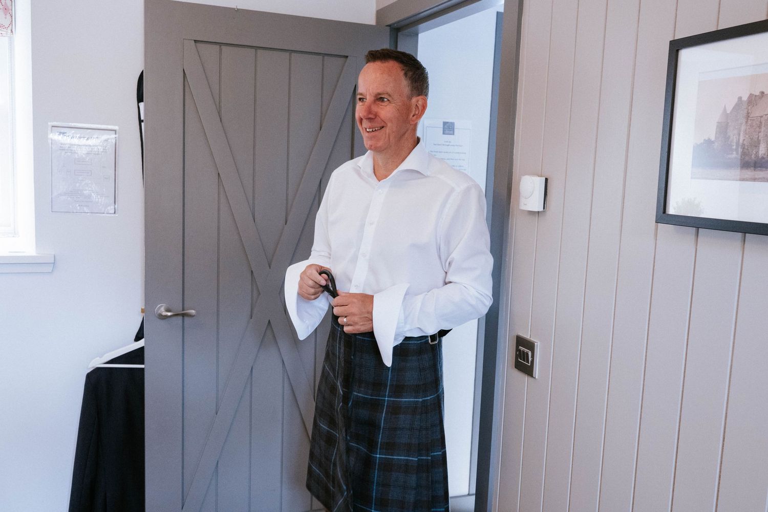 Person in white shirt and plaid kilt standing in a room with wooden paneled walls.