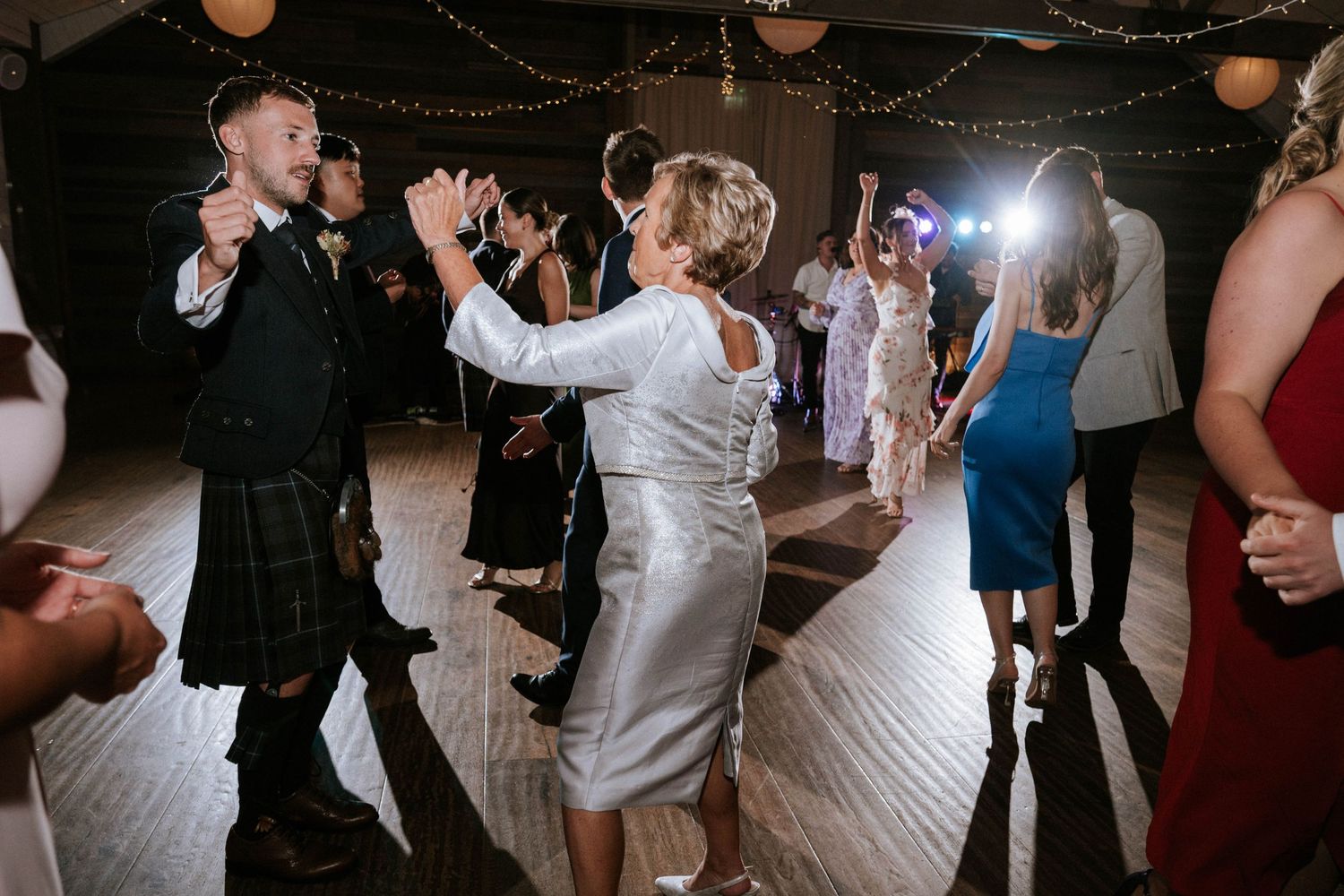 Guests dancing and celebrating at lively wedding reception under twinkling lights.