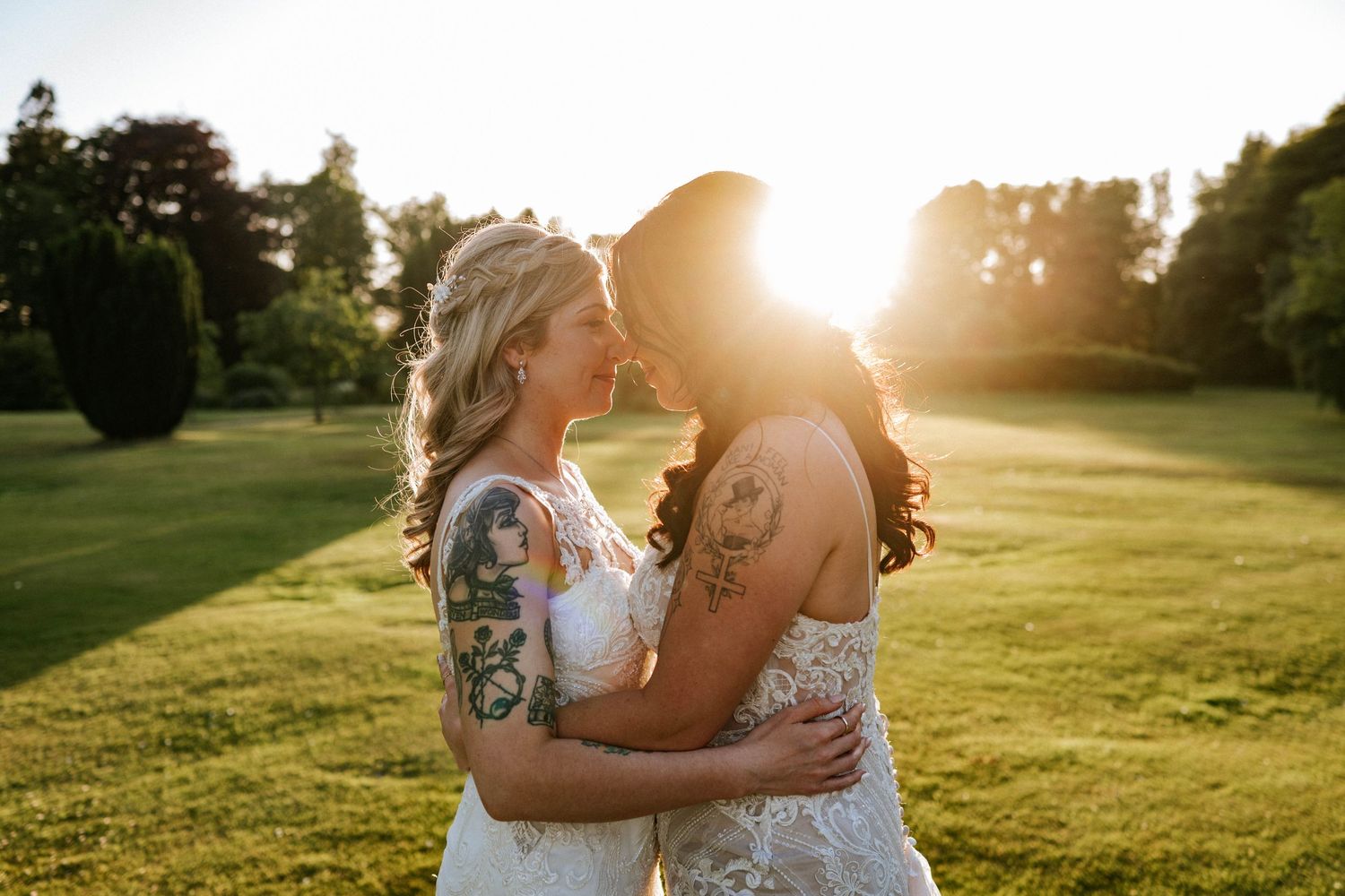 Aberdeen Wedding Photography. Two people in white wedding dresses embrace on a sunlit grassy hill during golden hour.