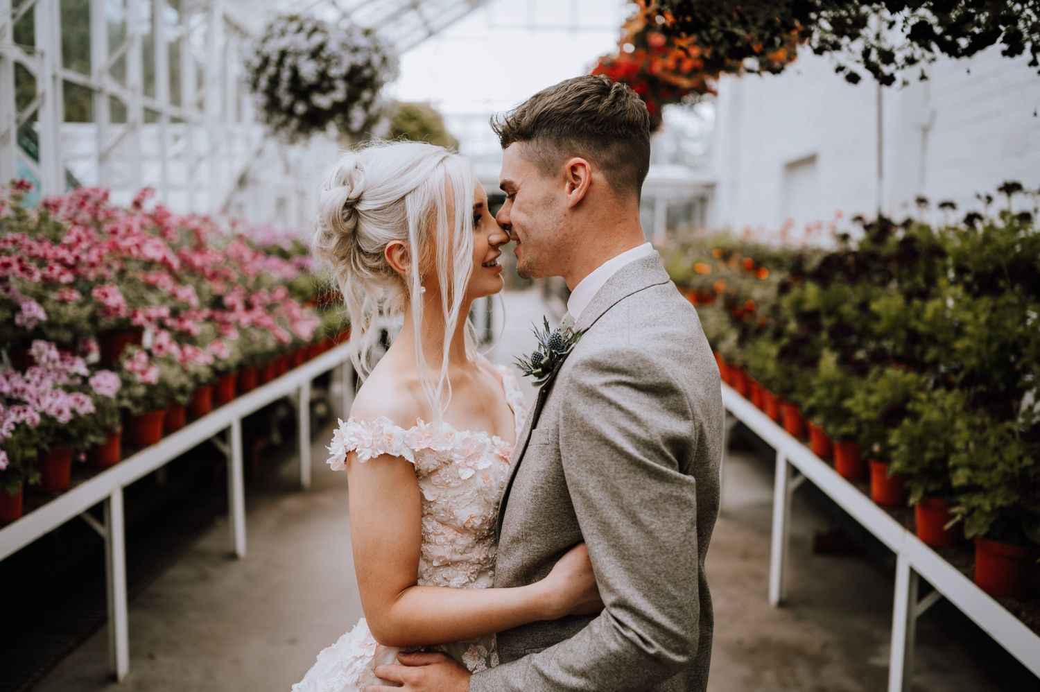Romantic wedding moment captured in a greenhouse walkway with blooming flowers.