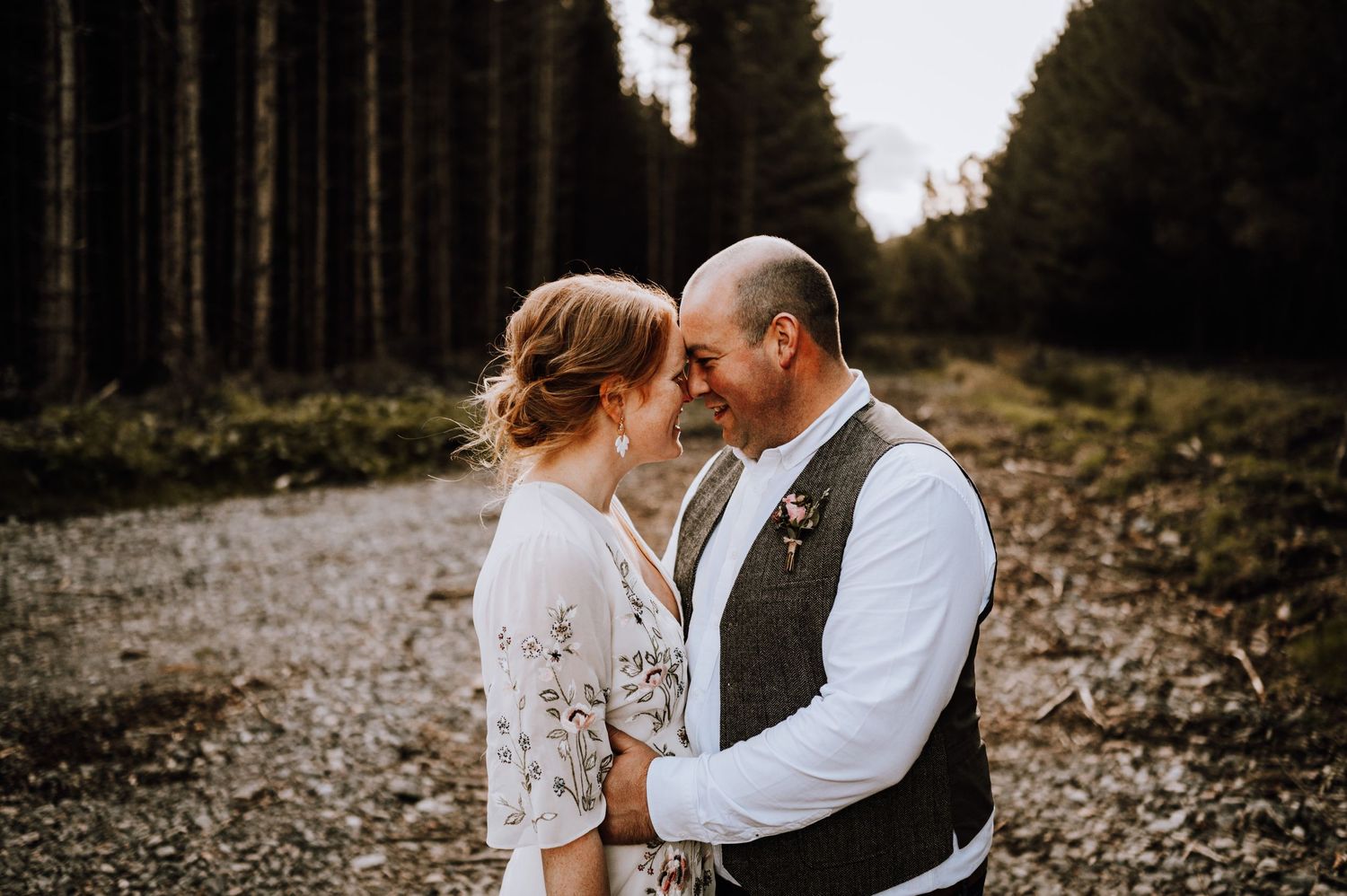 Romantic forest wedding portrait with couple embracing on a misty wooded path.