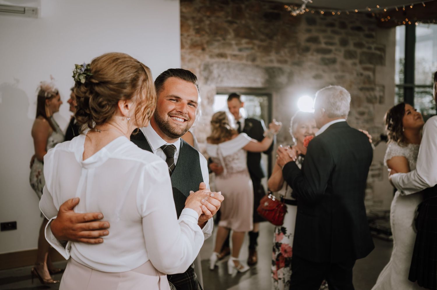Wedding celebration in a modern venue with string lights and exposed stone walls.