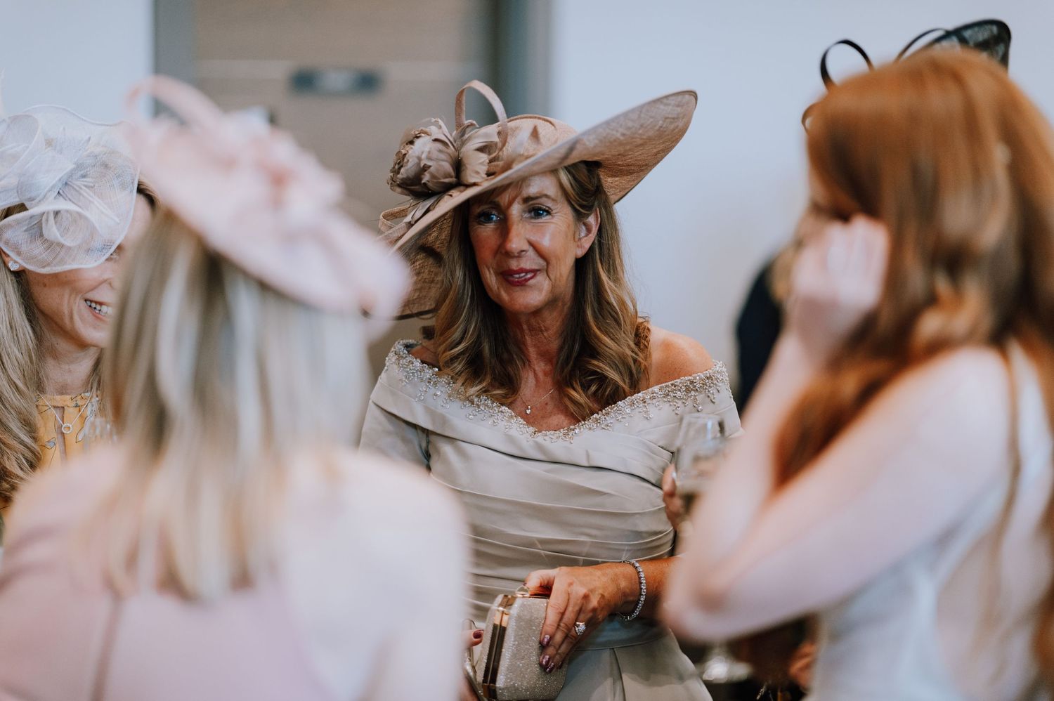 Elegant guests in formal attire and fancy hats socializing at an upscale event.