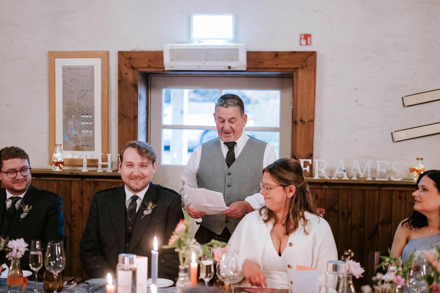Reception hall decorated with wooden panels and picture frames on walls during wedding celebration.