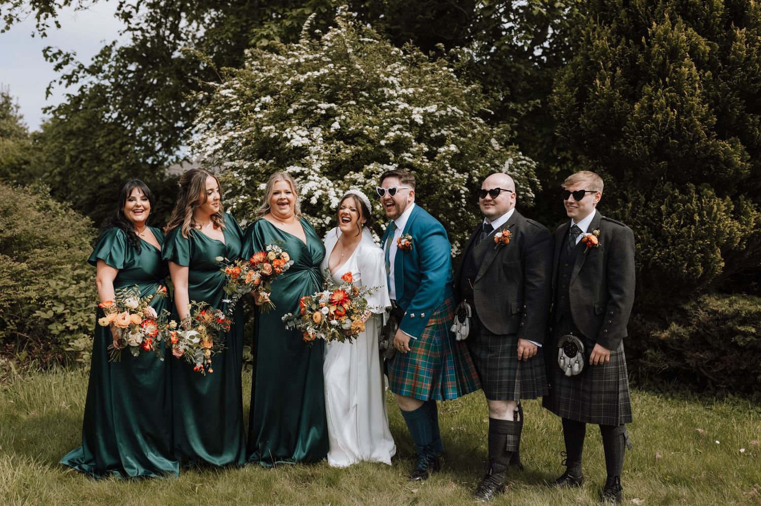 Scottish wedding party in traditional kilts and emerald dresses posing outdoors.