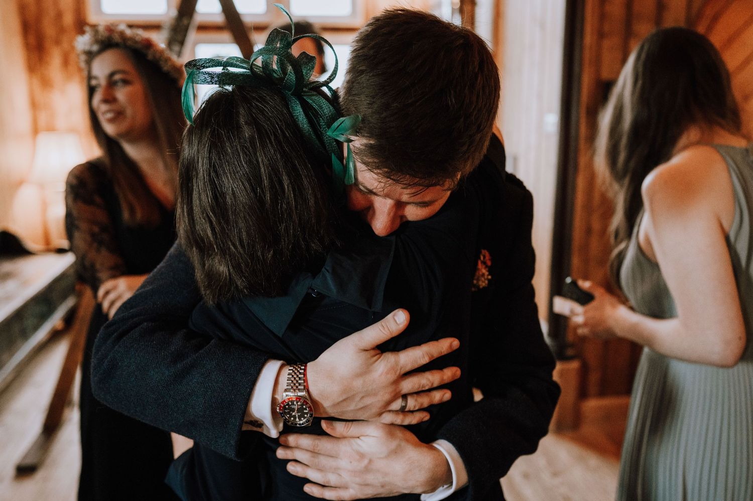 Emotional embrace between wedding attendees in a warmly lit wooden interior setting.