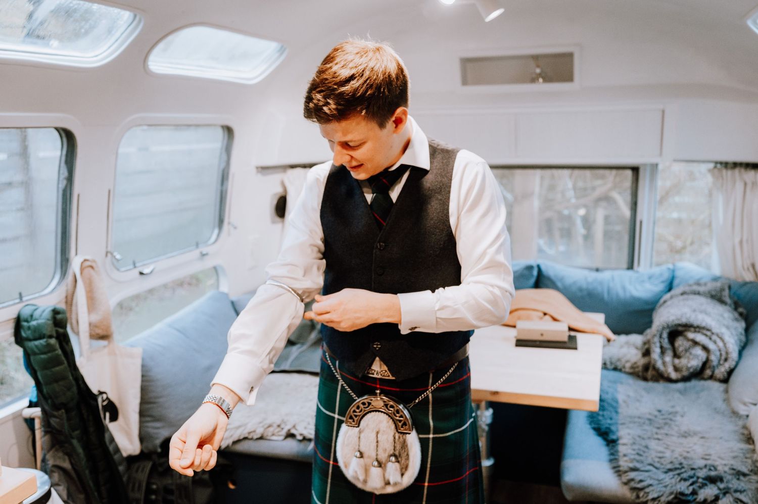 Person in formal Scottish attire preparing in mobile dressing room interior.