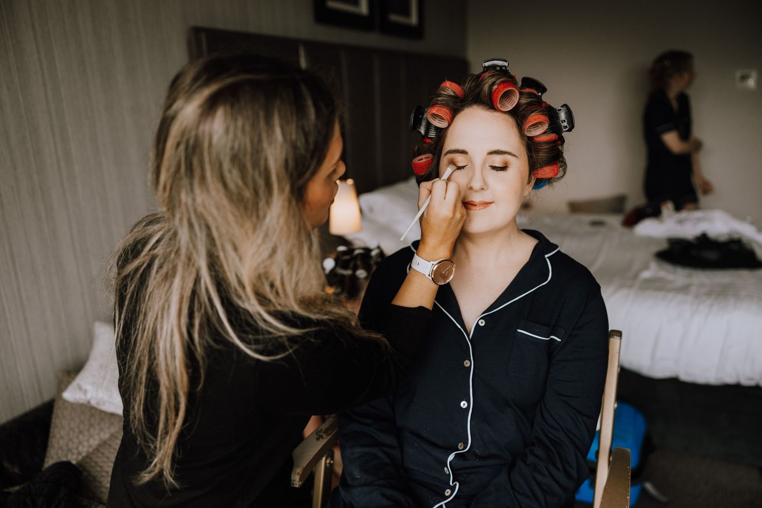 A makeup artist applies cosmetics to someone wearing orange hair rollers.