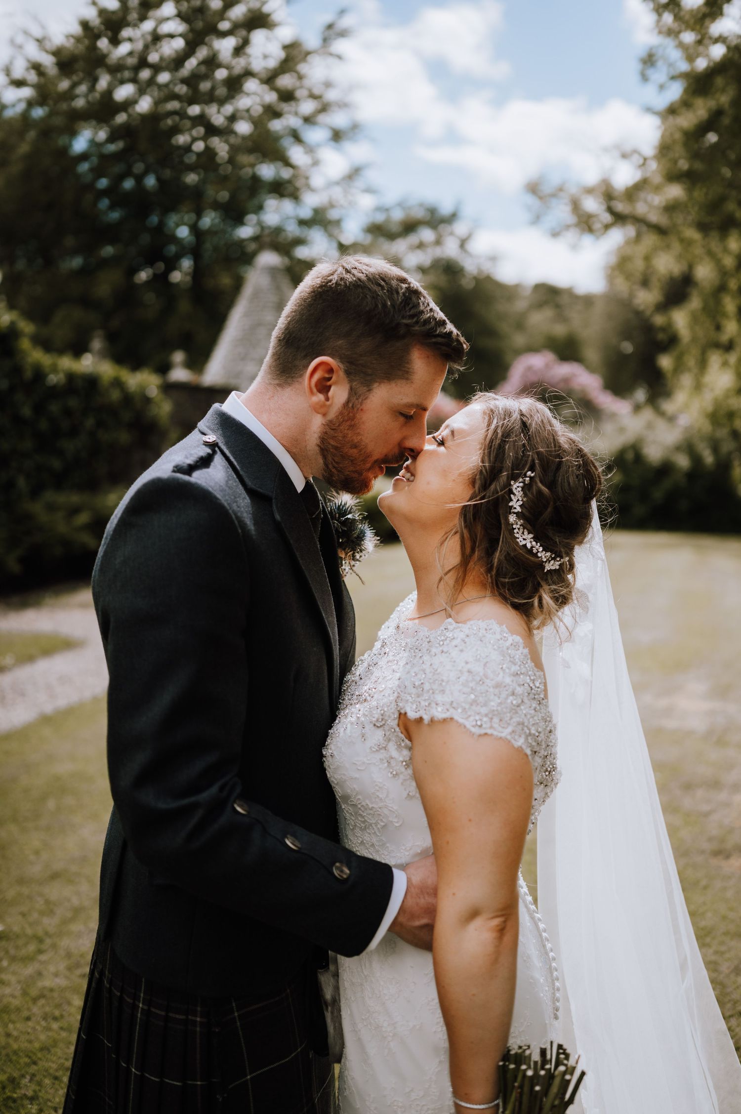 Newlyweds share a tender moment outdoors with the groom wearing a traditional Scottish kilt.