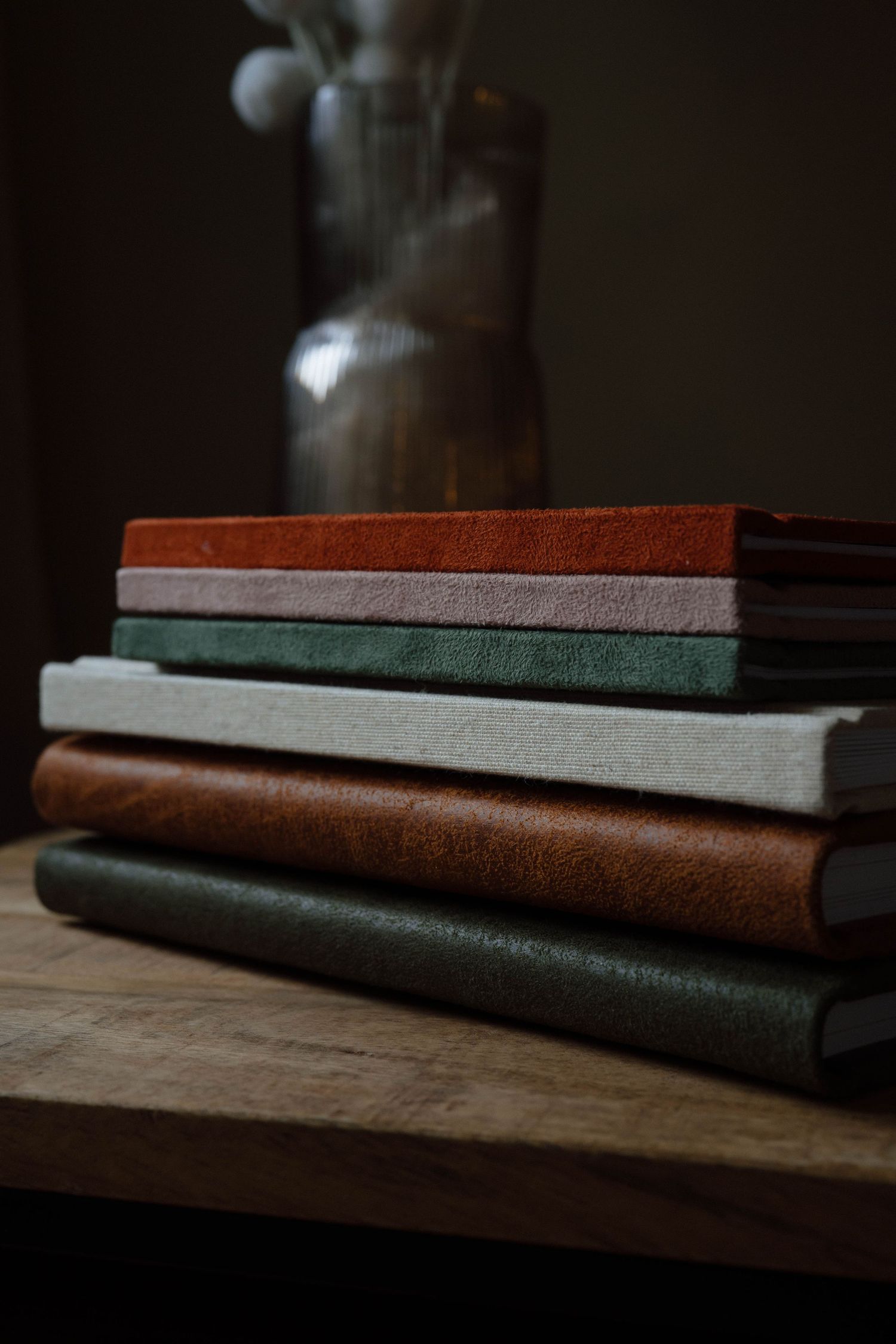 Dark leather photo albums stacked horizontally on a wooden surface in moody lighting.
