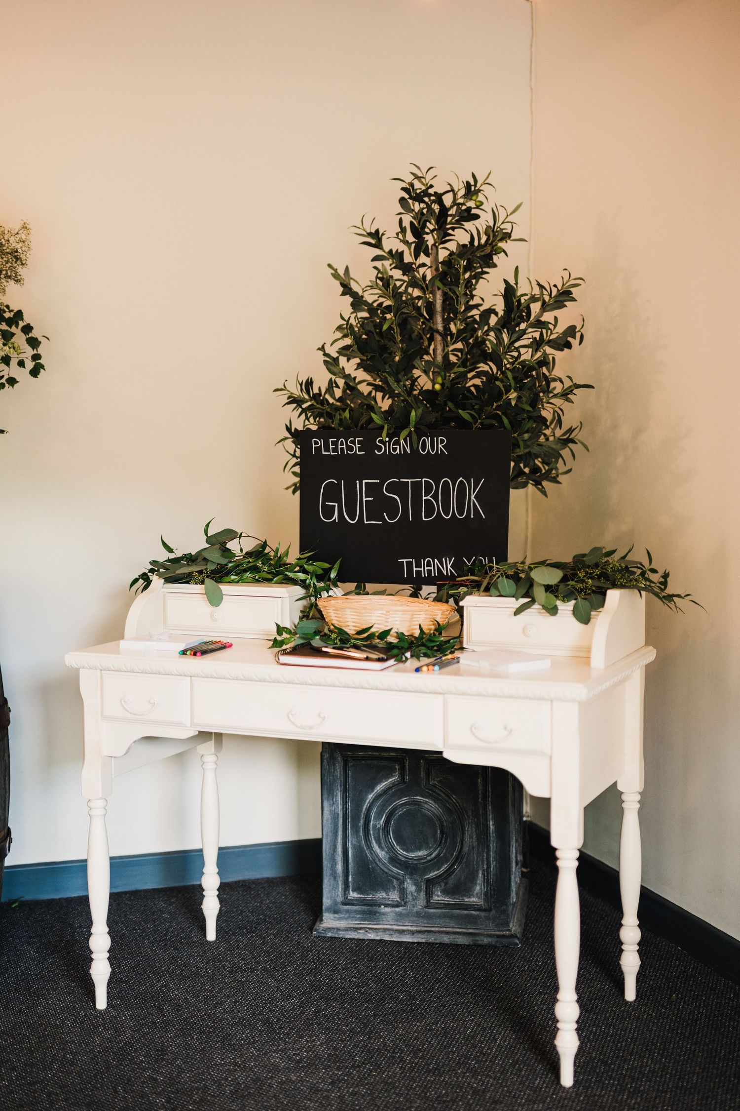 White vintage table with chalkboard guestbook sign and greenery decorations.