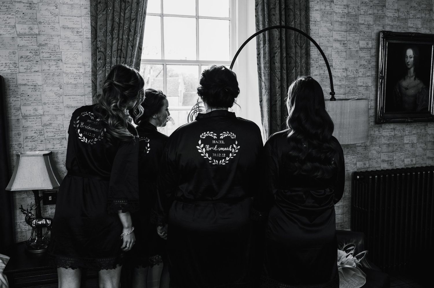 Three people in black outfits stand in silhouette against a bright window with a vintage lamp in the corner.