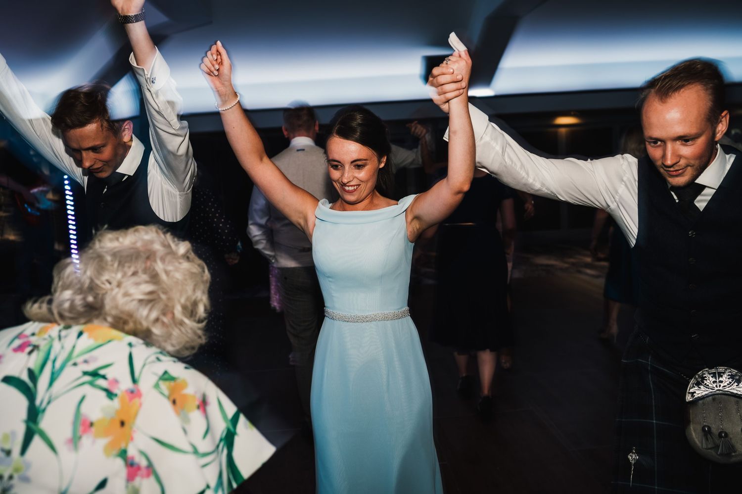 Wedding guests dance together with raised arms during a festive celebration.