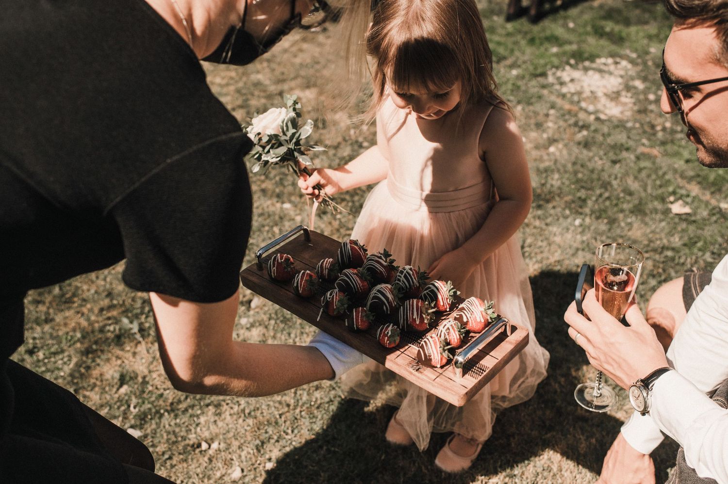 Wedding guests examine chocolates or treats being served at an outdoor reception.