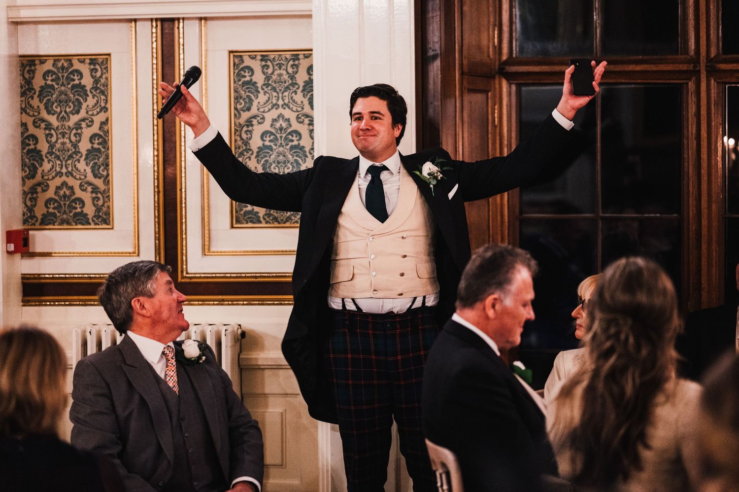 Speaker stands dramatically with arms raised during formal dinner toast.