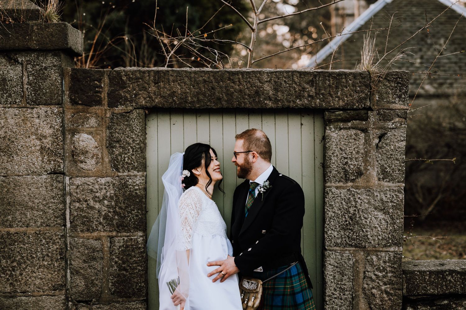 A tender moment between newlyweds framed by a stone archway on their wedding day.