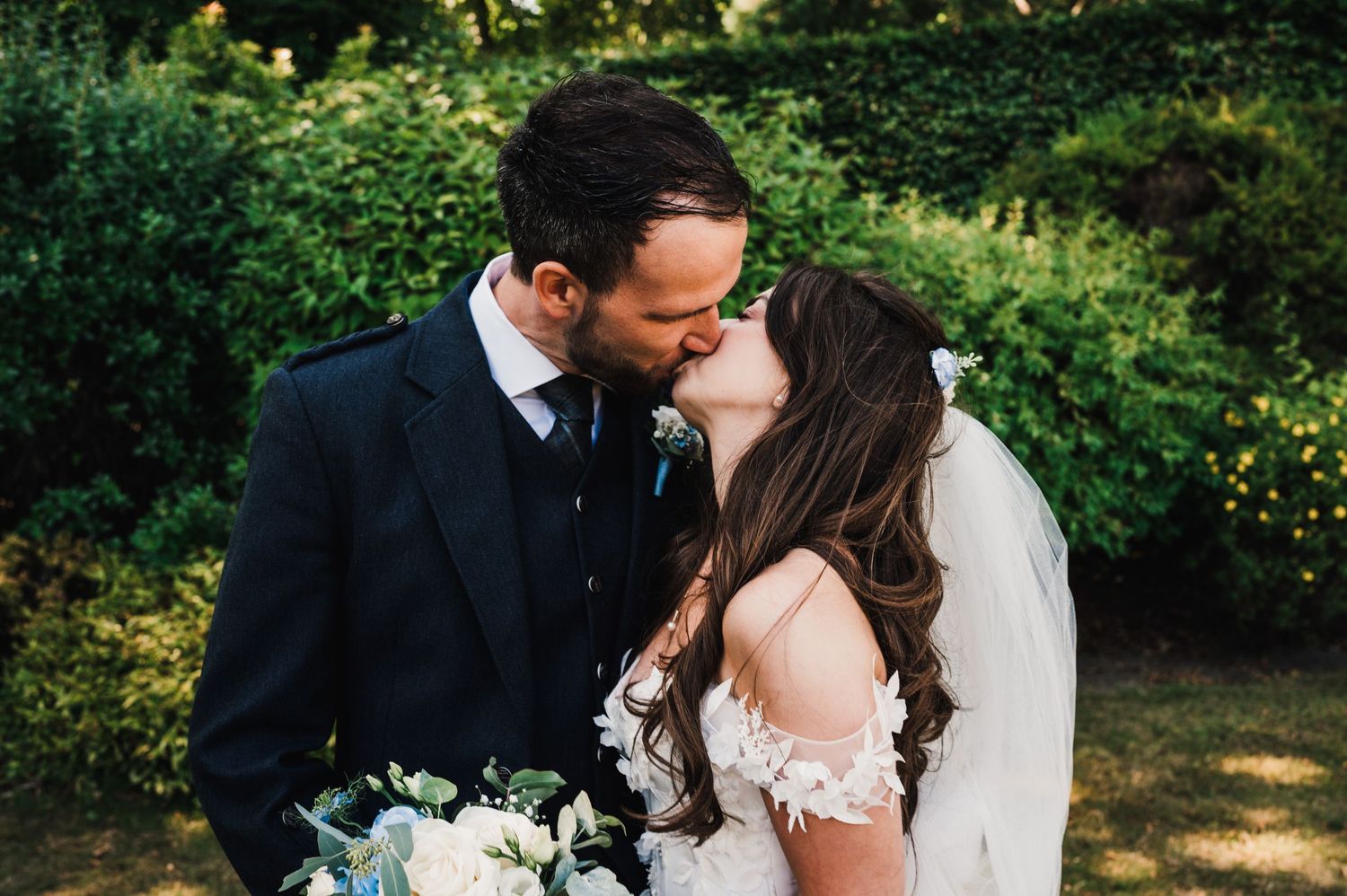 Intimate wedding couple moment in garden with traditional Scottish and bridal attire.