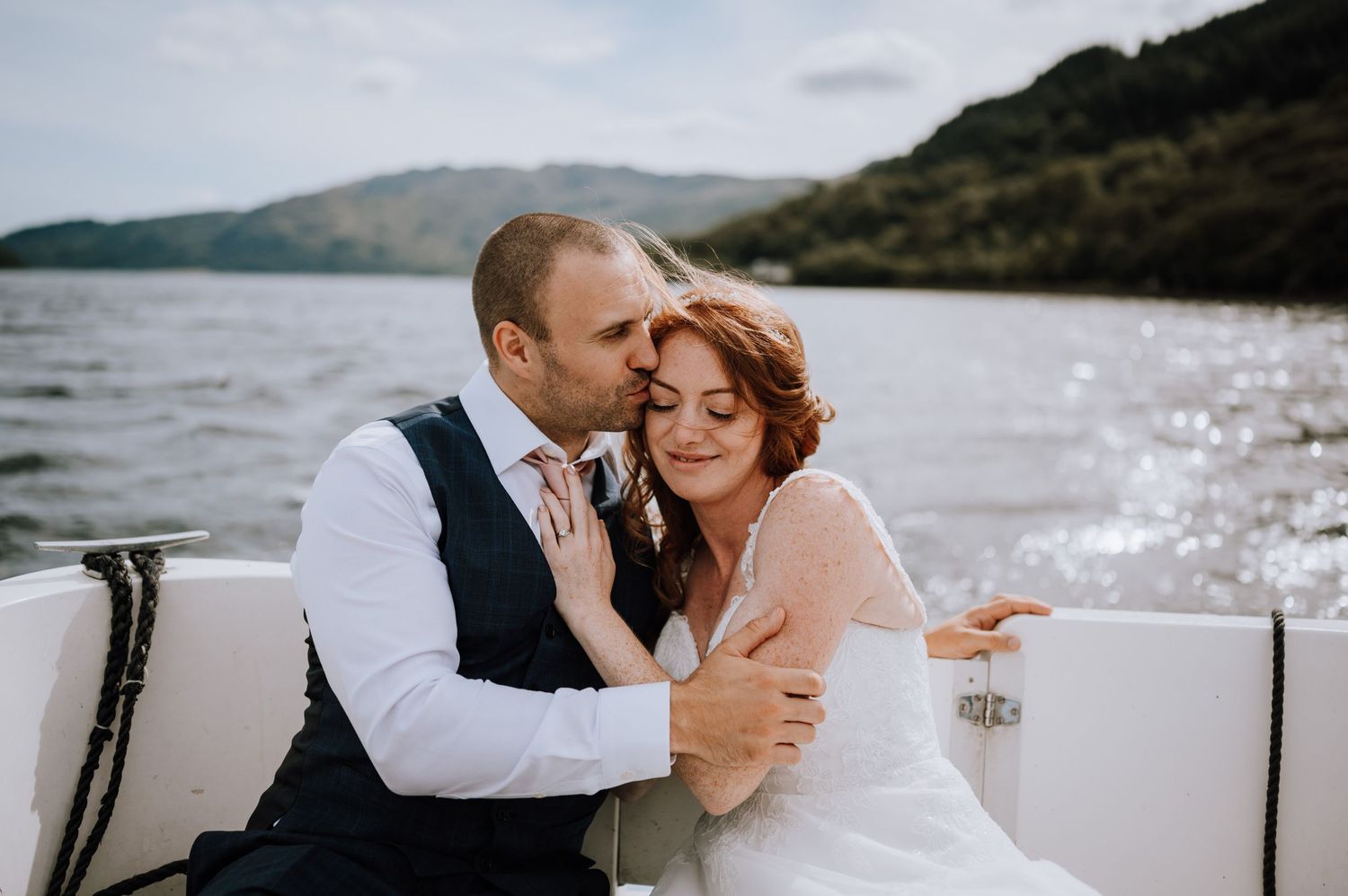 A sweet embrace captured on a boat with sparkling water and mountains in the background.