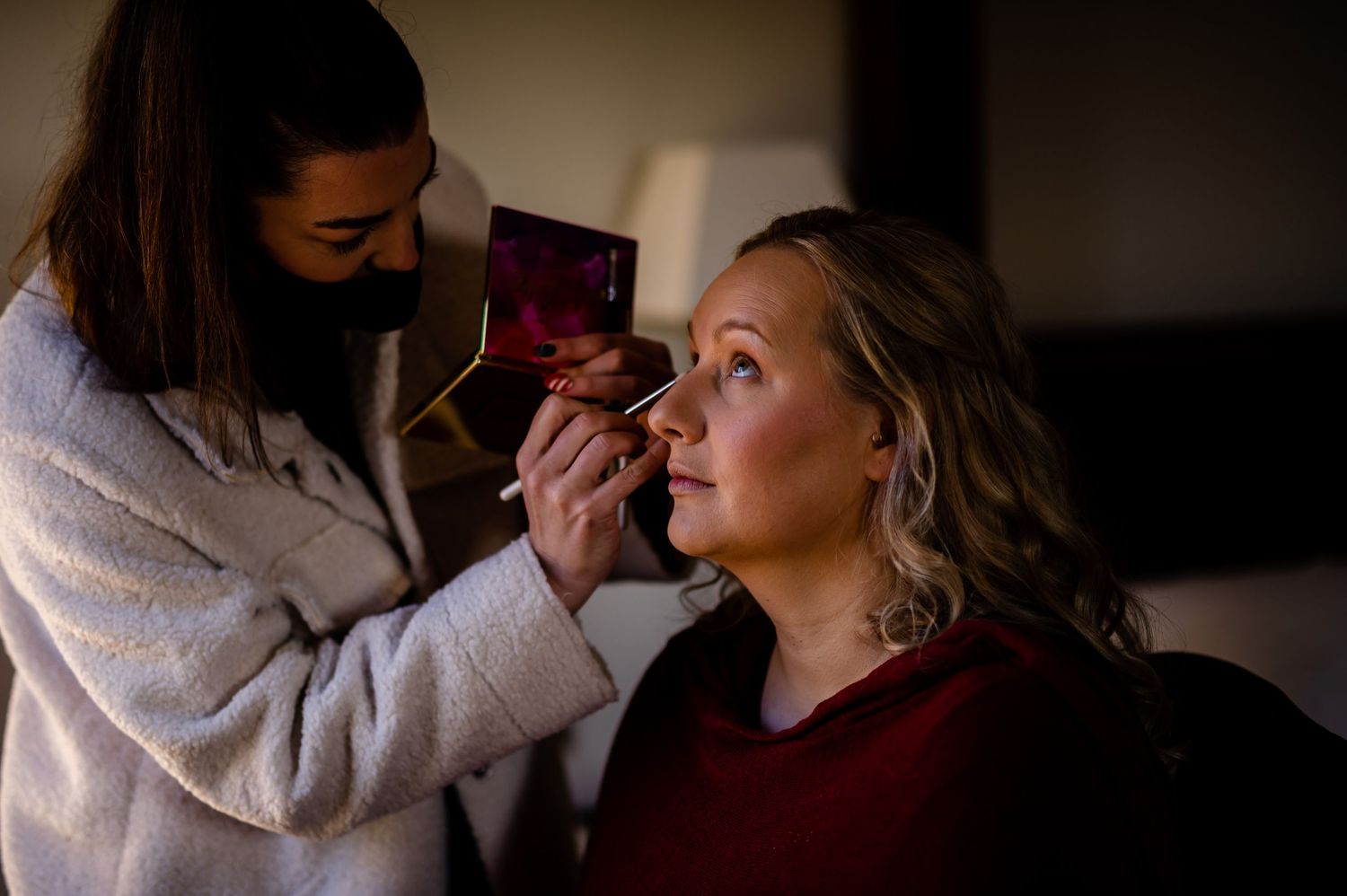 Makeup application scene in soft, dramatic lighting.