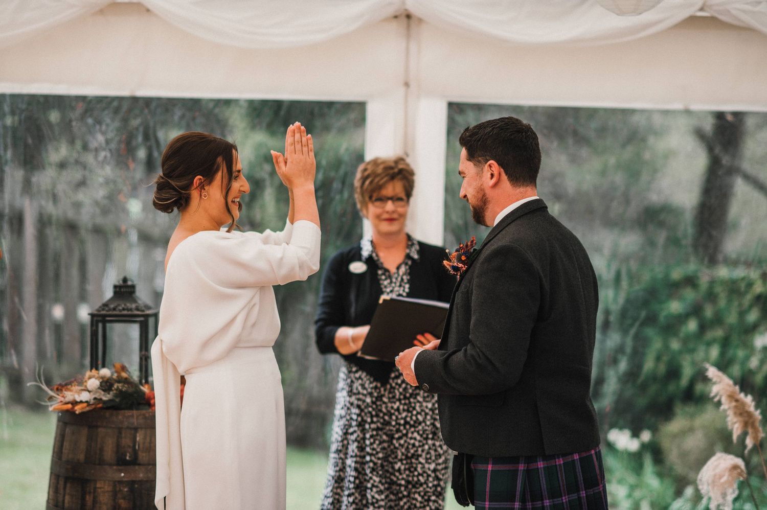 Wedding couple celebrating during ceremony with raised hands in white tent setting.