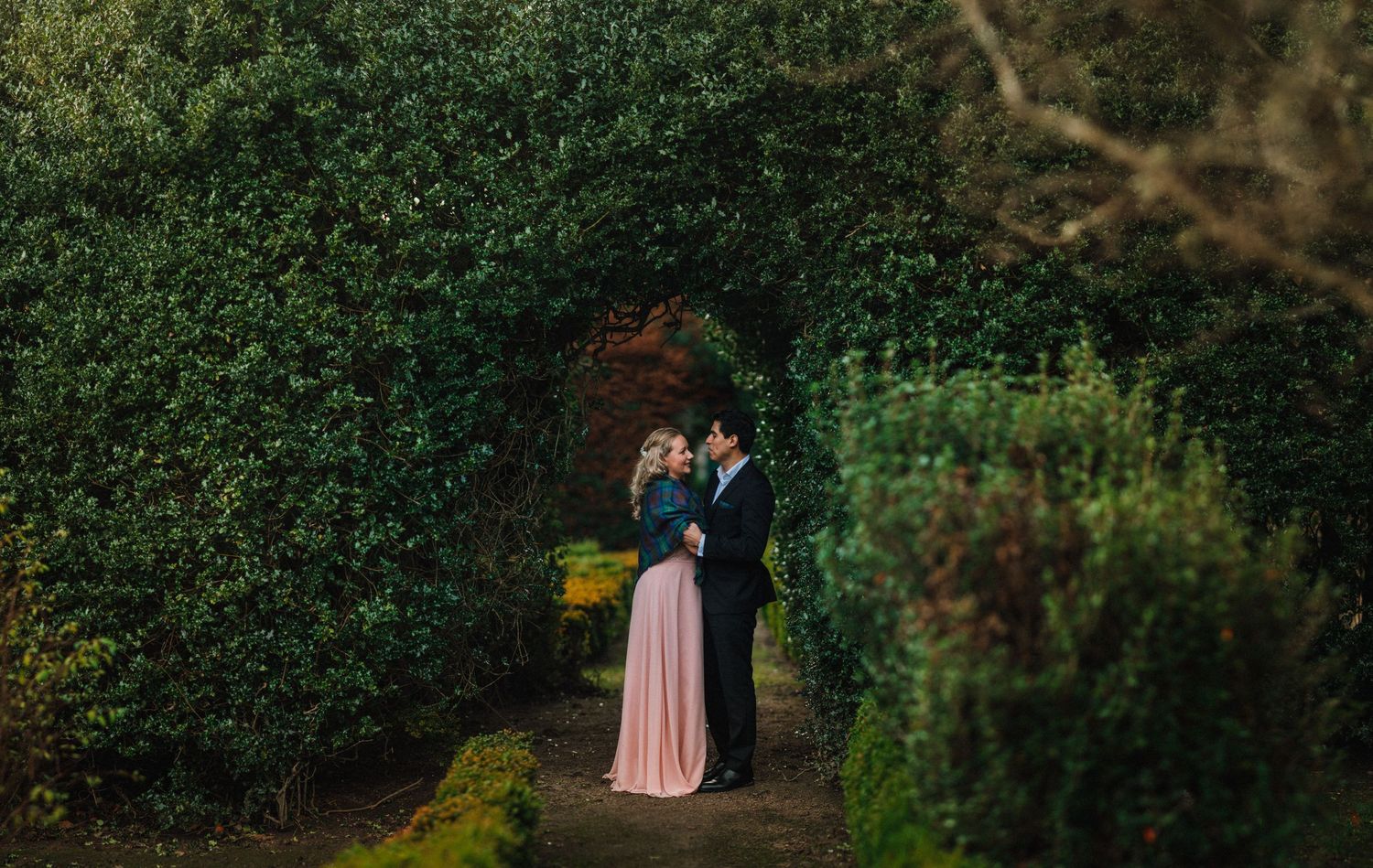 A romantic moment captured between a couple in a lush garden setting with moss-covered ground.