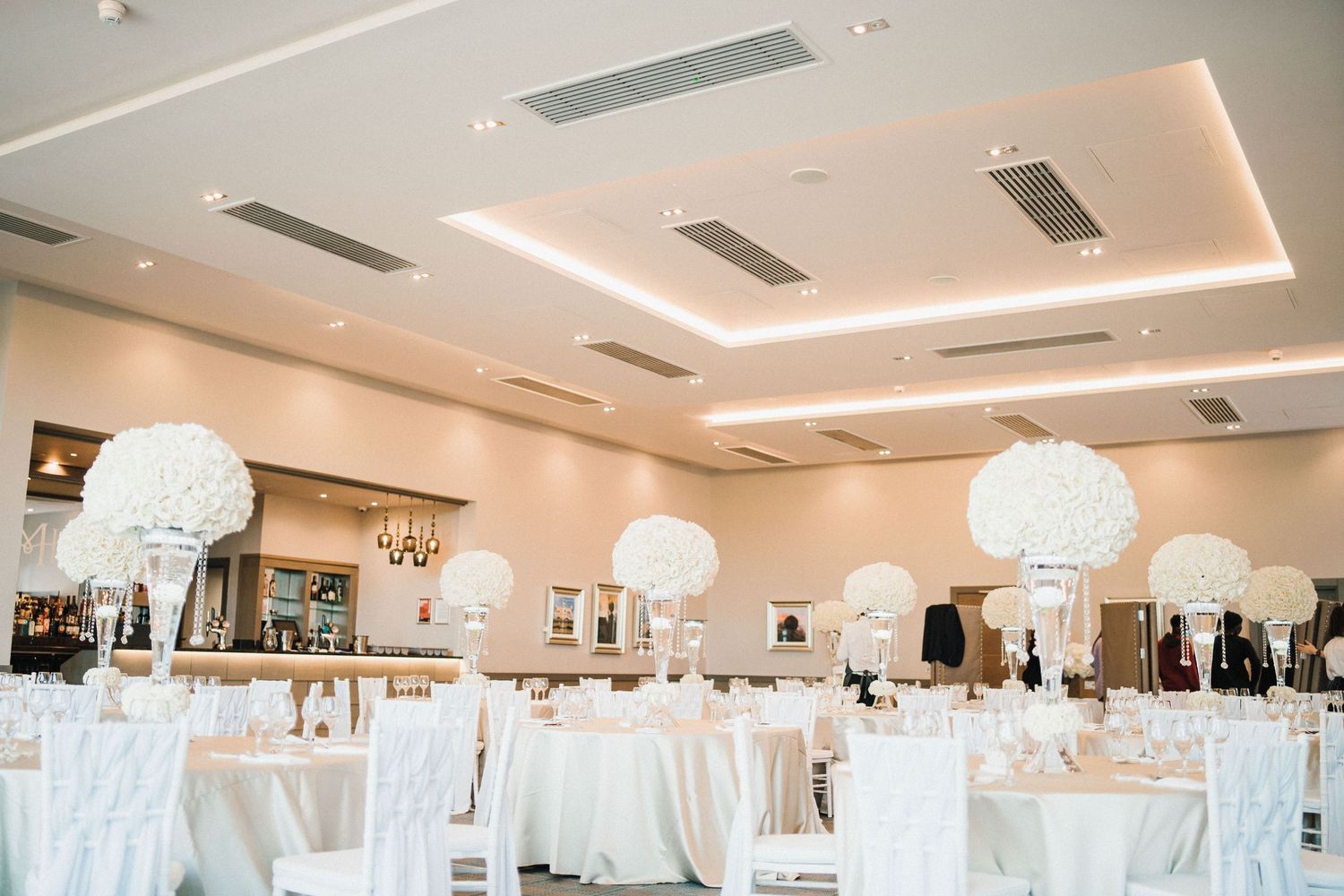 Elegant white wedding reception venue with tall floral centerpieces and dramatic lighting.