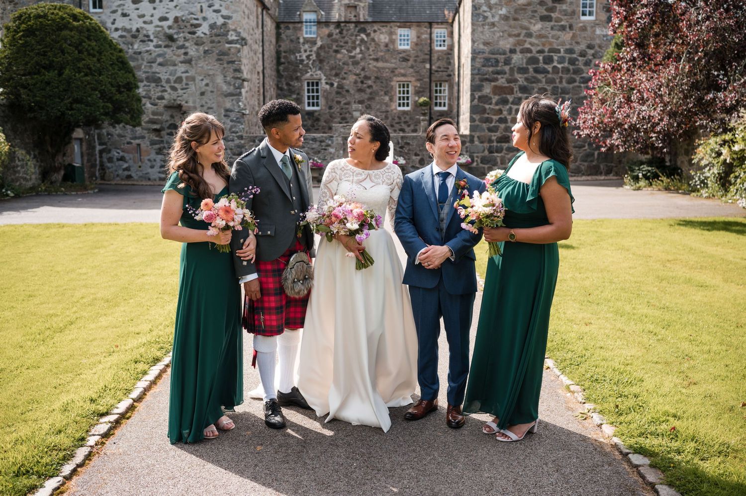 Wedding party members in white and emerald green attire pose together on church grounds.