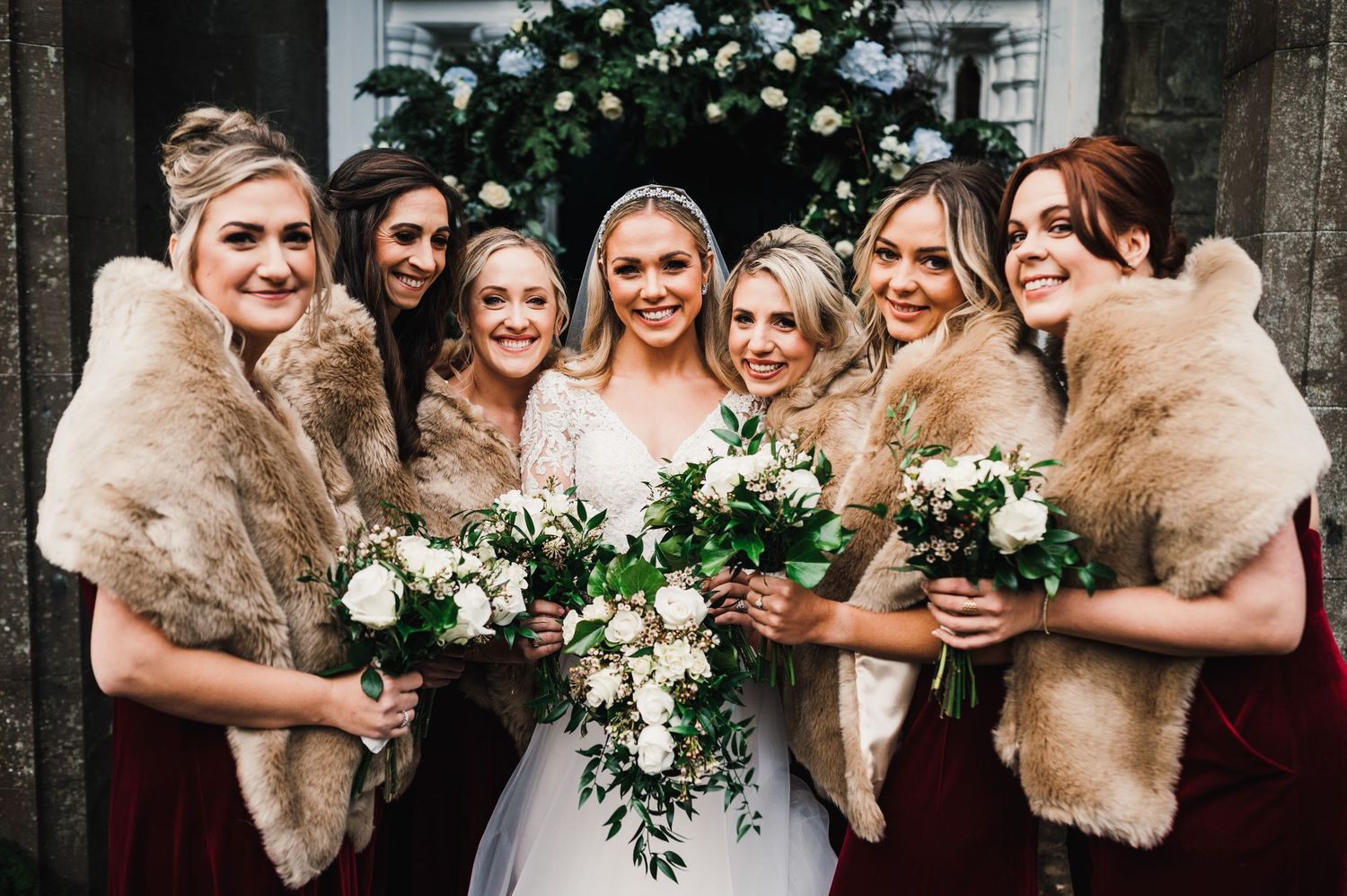 Aberdeen Wedding Photography. Bridesmaids in elegant dresses with fur shawls pose together holding white floral bouquets.