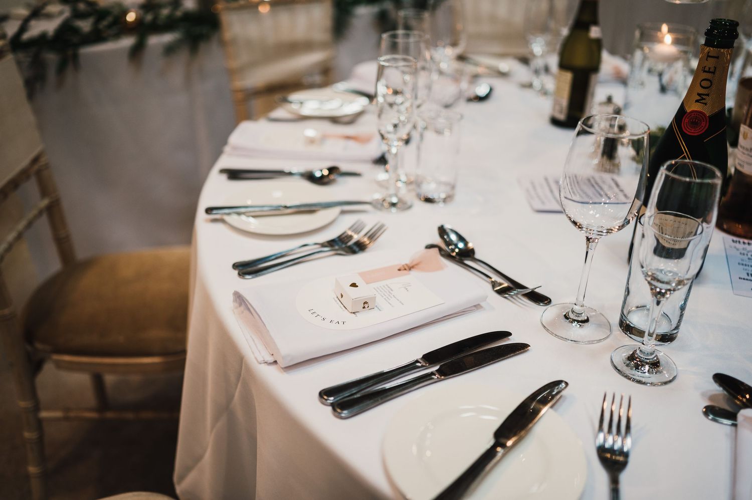 Elegant table settings with wine glasses and cutlery on white tablecloths at a formal event.