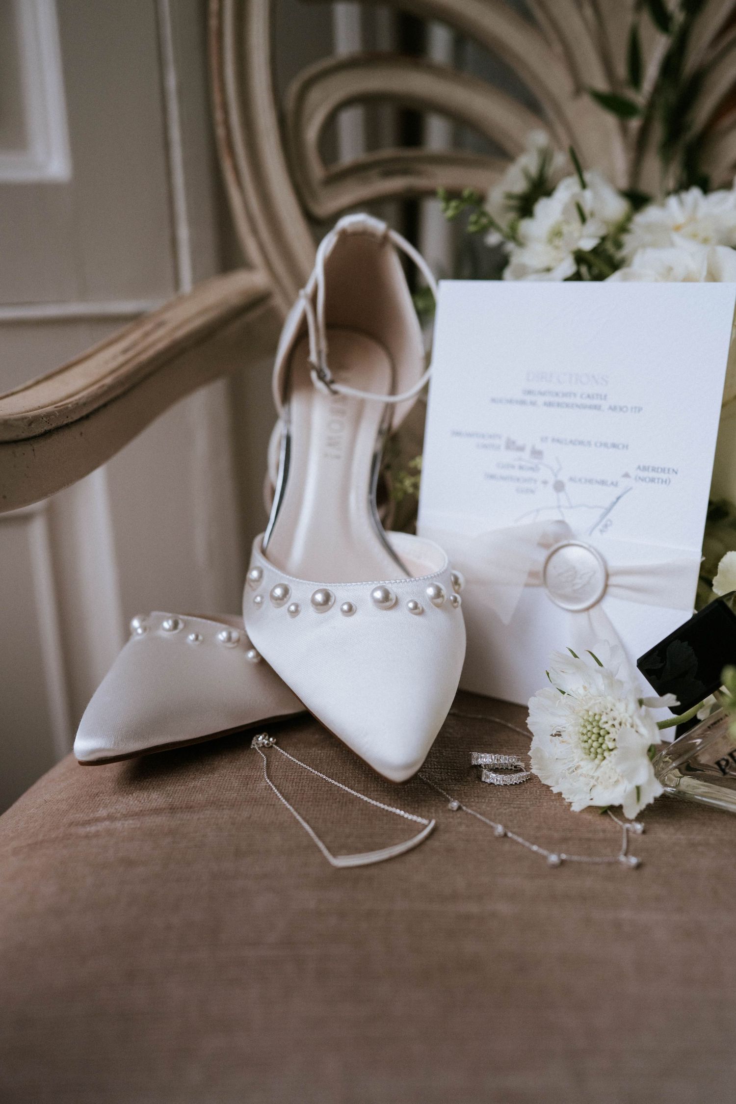 Elegant white bridal shoes with pearl embellishments and delicate straps displayed on a brown surface.