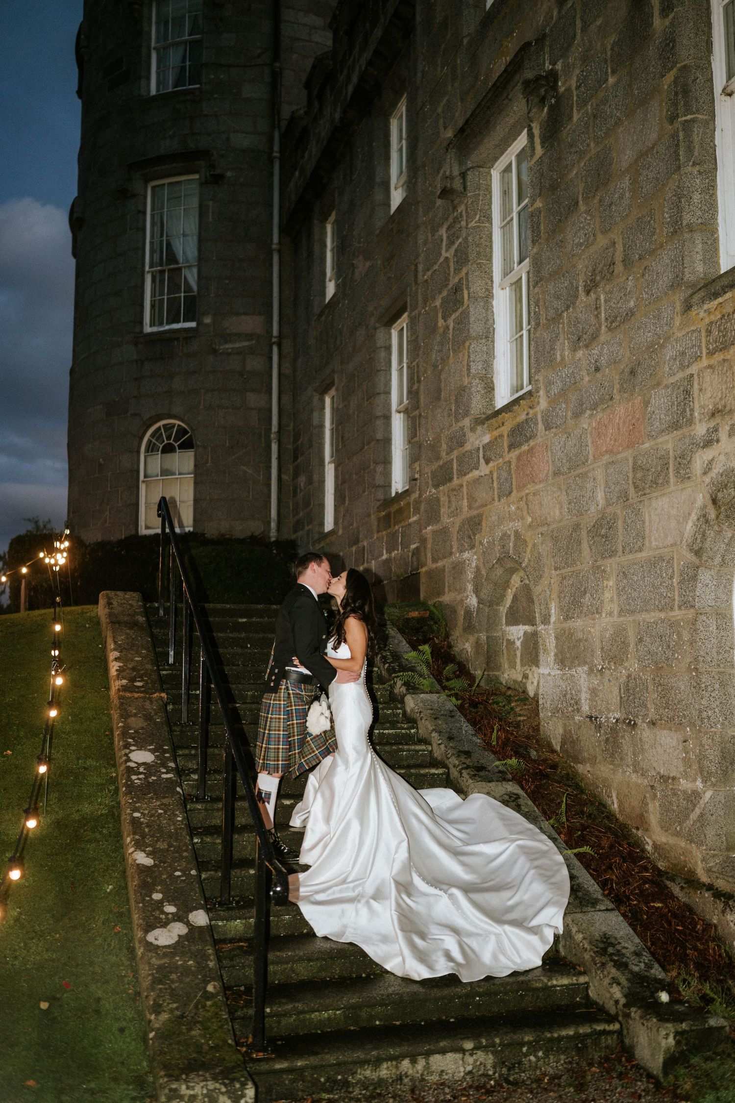 Dramatic nighttime wedding photos against stone castle walls with string lights.