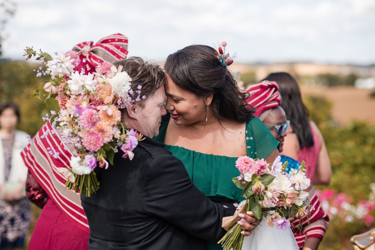 Wedding party members embrace and celebrate with pink floral bouquets.