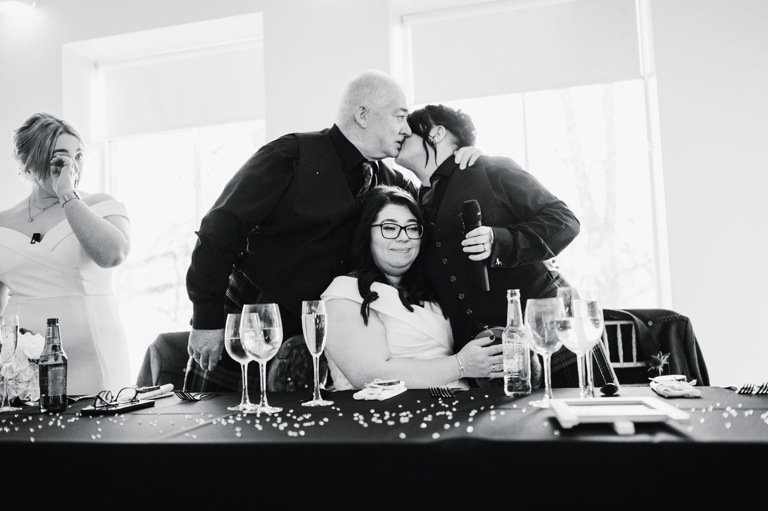 Logie House Wedding Photography. Intimate black and white photo of guests sharing a moment at a wedding reception table with wine glasses.
