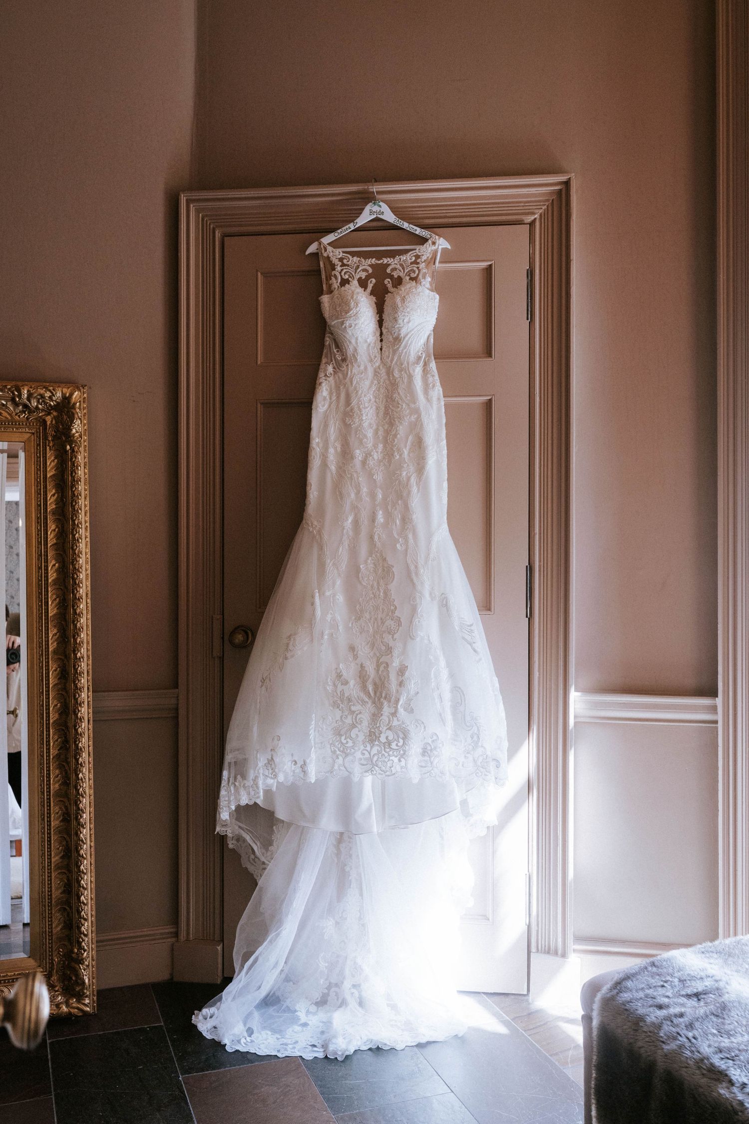 Fasque Castle Wedding Photography. A white lace wedding gown hangs elegantly against a neutral-toned wall.
