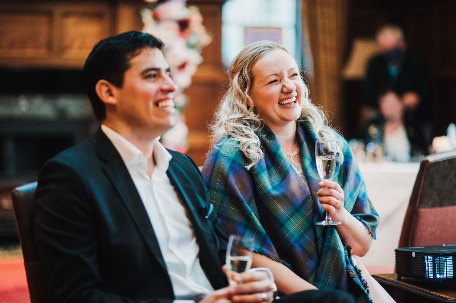 A couple laughs while enjoying drinks together at a celebration.