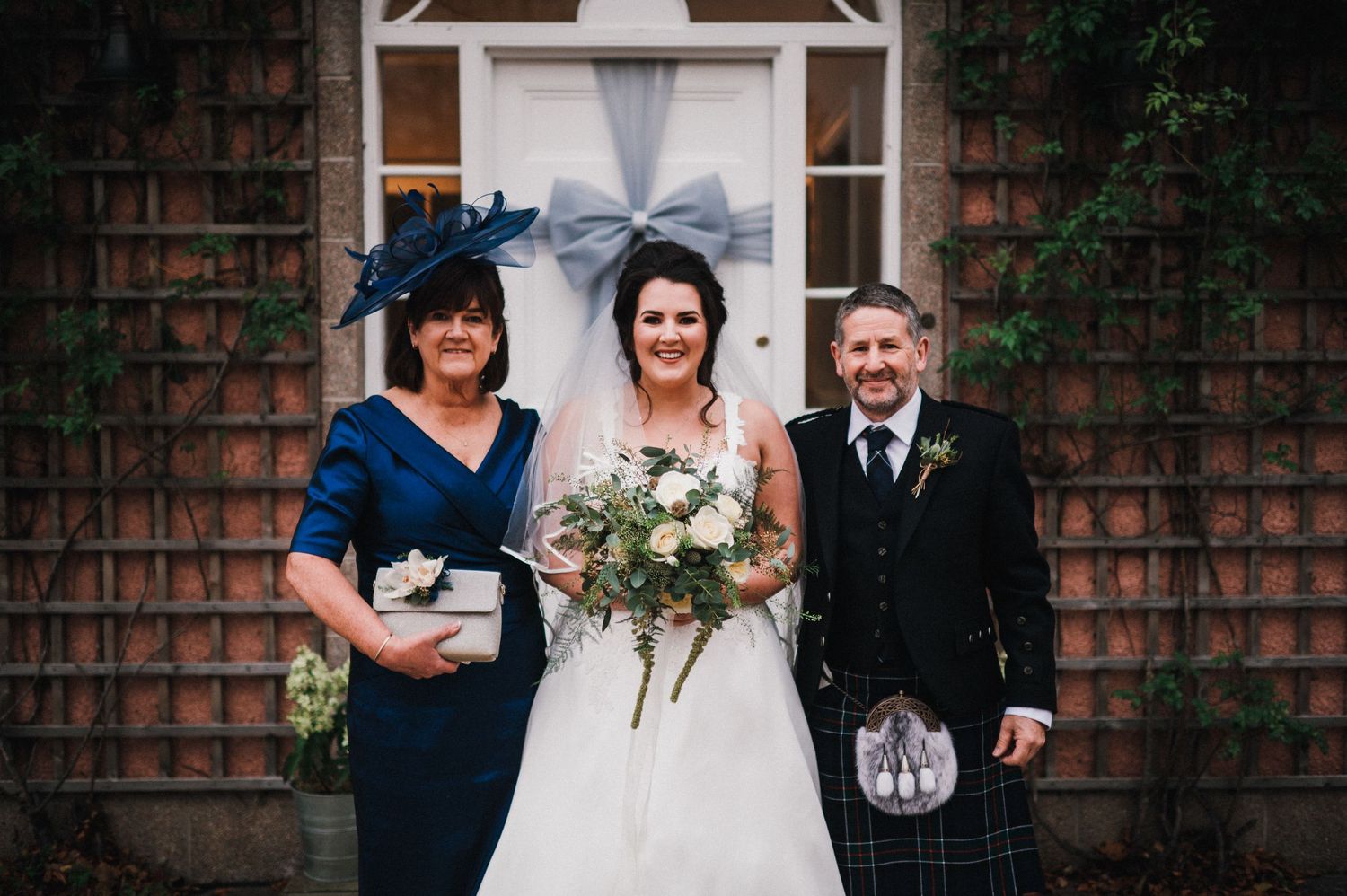 Wedding party poses in front of brick building with lattice and decorative white bow.