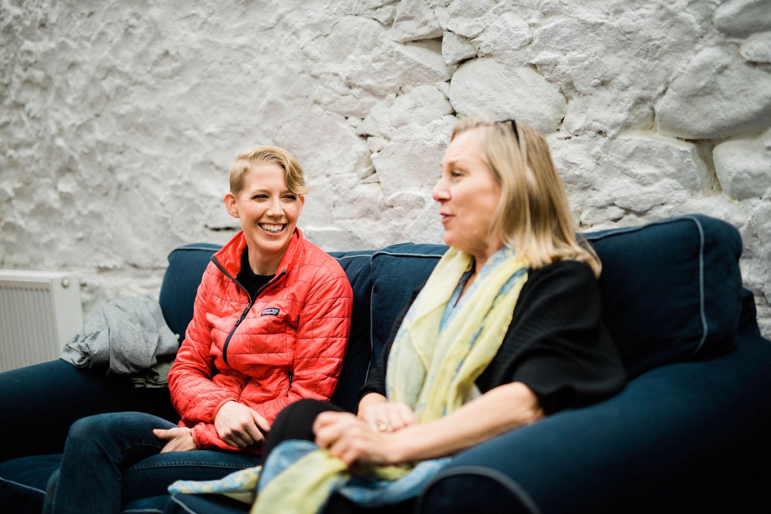 Casual conversation between two people seated on a blue couch against white stone wall.