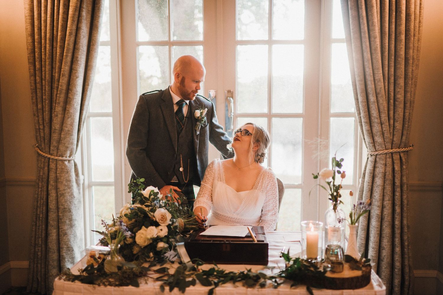 Candid moment of newlyweds at their wedding signing table by a bright window.