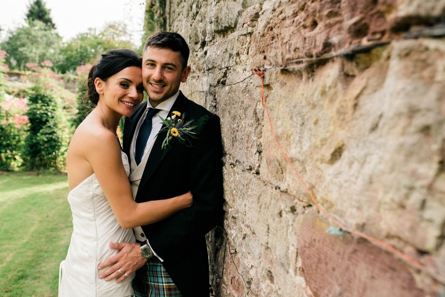 A romantic embrace against a rustic stone wall in a garden setting.