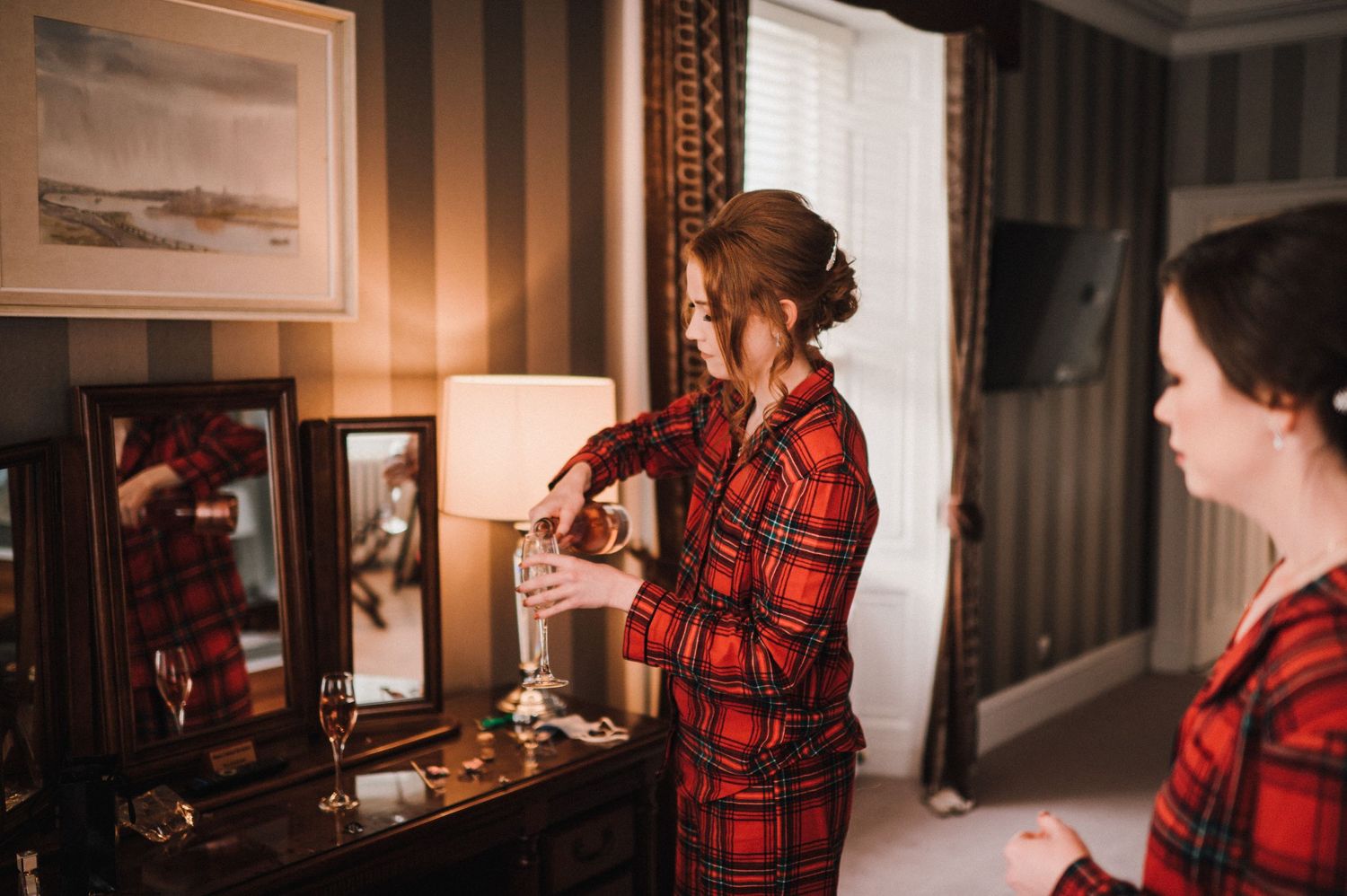 Two people in red plaid robes preparing at a vanity mirror.