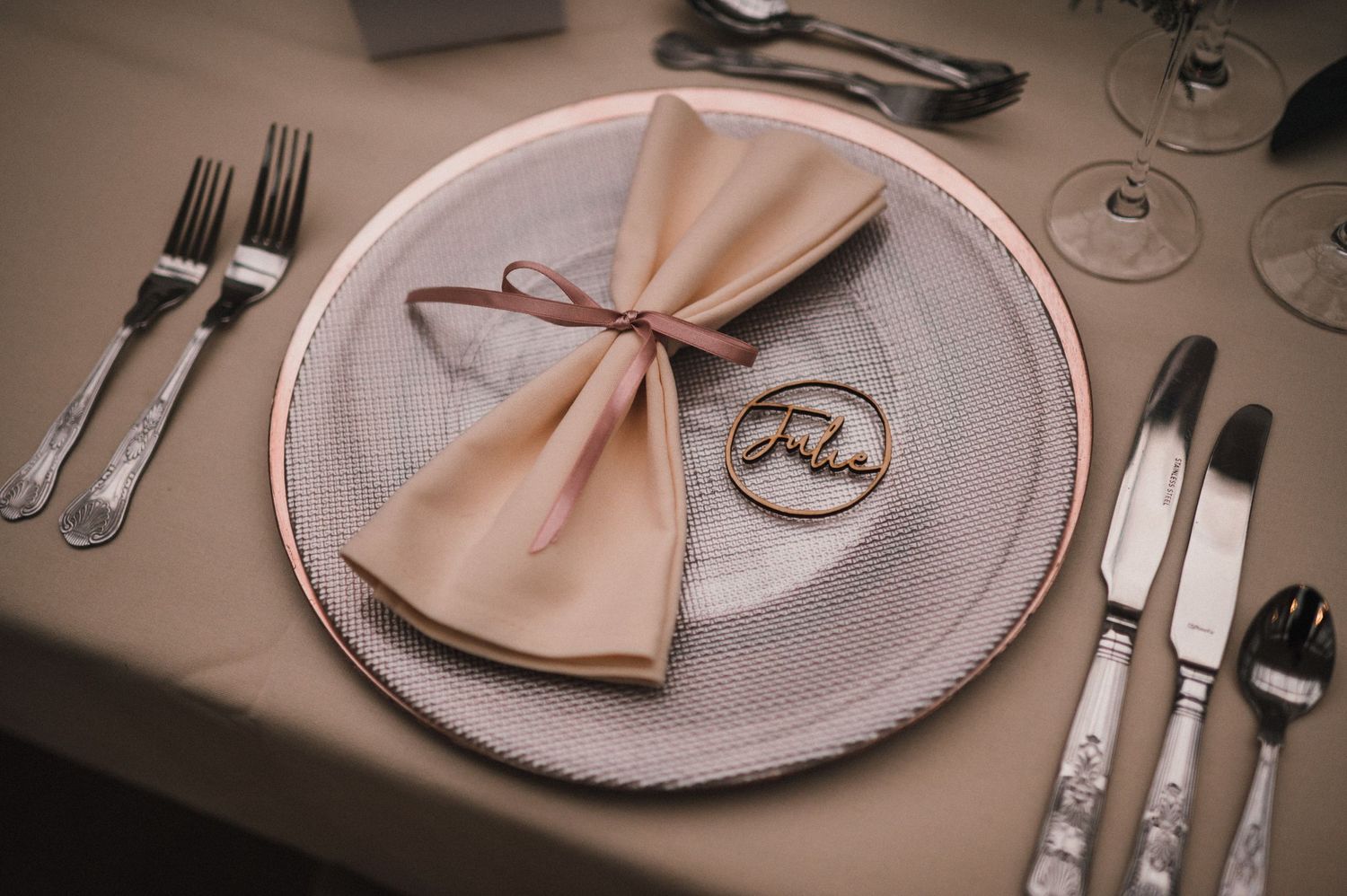 Elegant place setting with beige napkin bow on textured white plate with monogrammed detail.