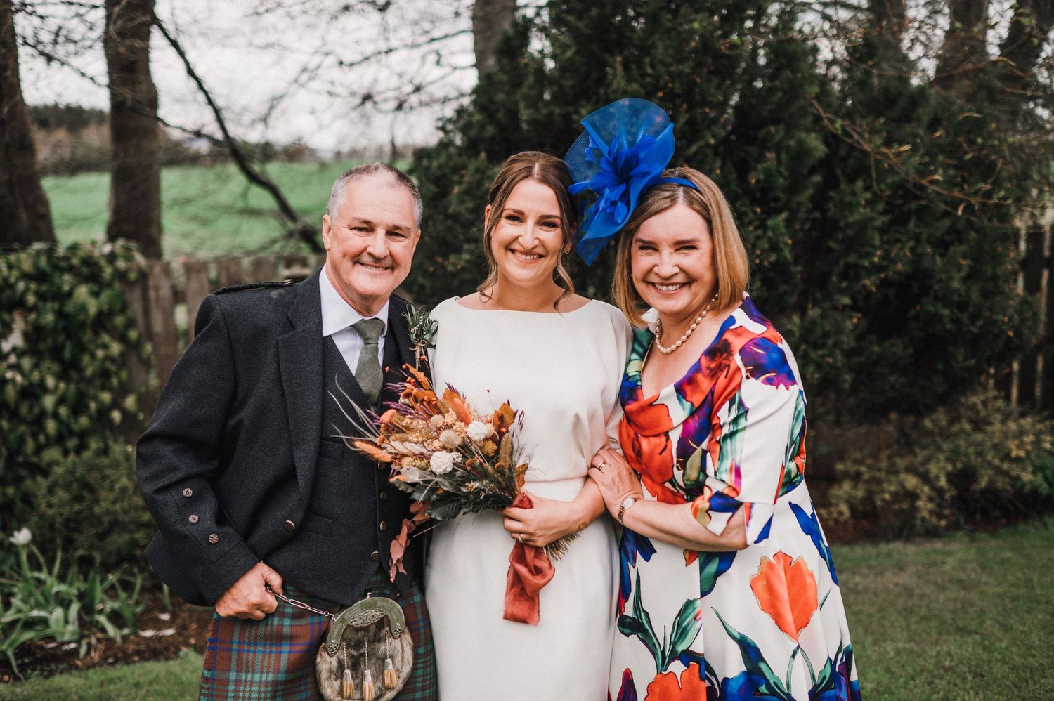 Wedding celebration with elegant attire including Scottish kilt and vibrant blue fascinator.