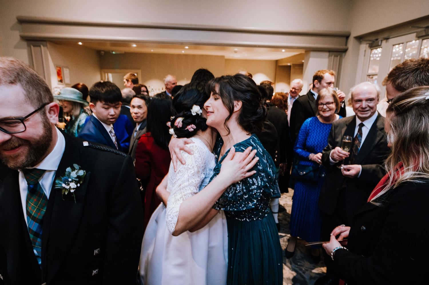 A crowded indoor reception shows guests embracing and celebrating during a joyous wedding event.
