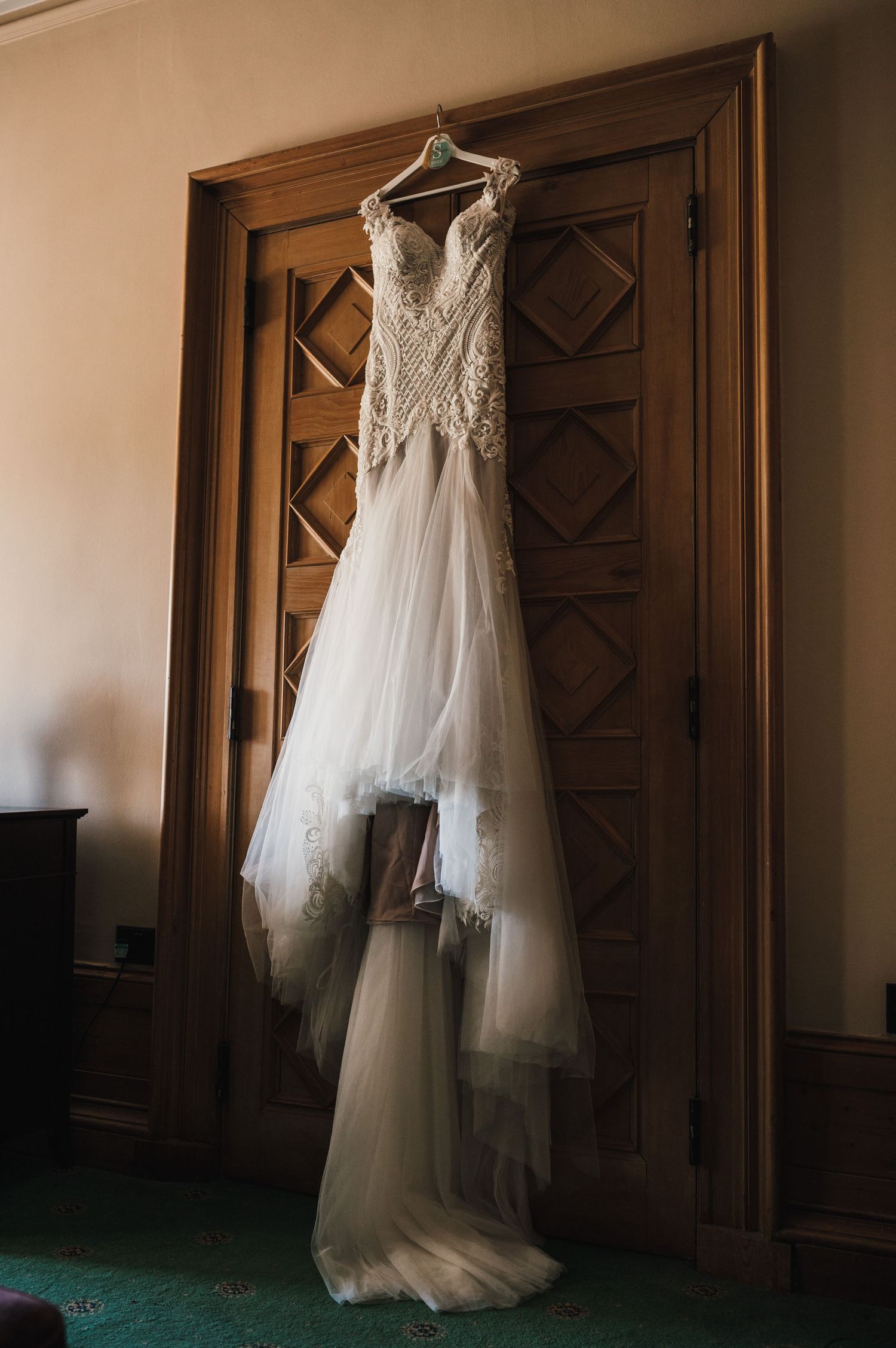 Wedding dress with lace bodice and tulle skirt hanging against ornate wooden door.